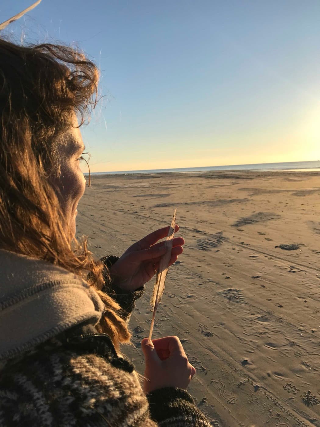 Marieke on the beach at sunset, holding a blade of grass