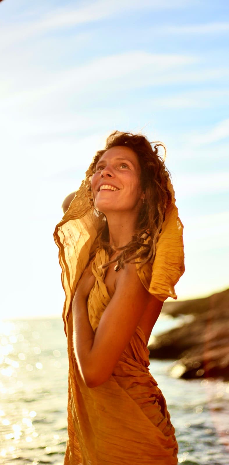 Marieke by the sea in a golden yellow dress, looking up at the sun